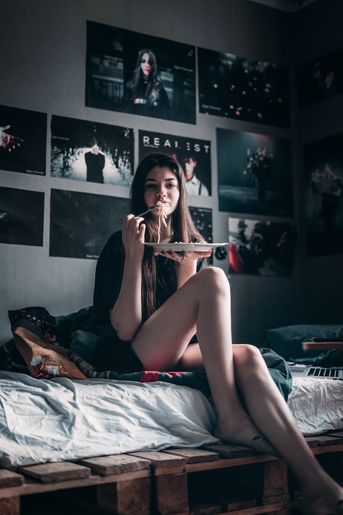 Woman in Black Tank Top Sitting on Bed Holding a Plate